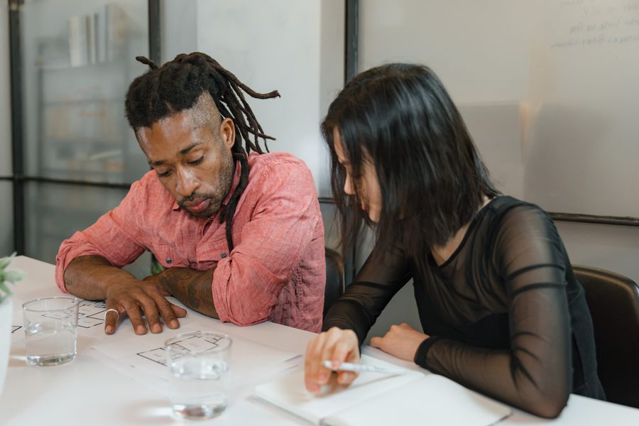 man and woman sitting at table with blueprints at office