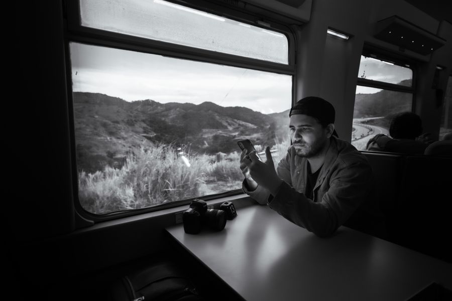 Man using a smartphone on a train journey through scenic landscape. — The departure board flips: gate found, lounge located, all on the eSIM.