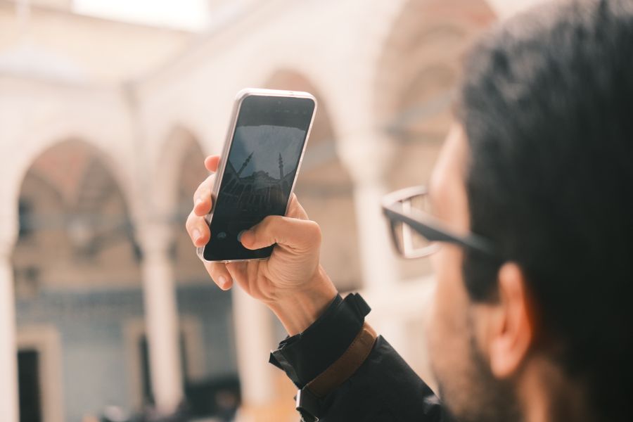 An adult male photographs a mosque using a smartphone outdoors with a focus on capturing architecture. — Country Connectivity Fact Sheet remembers, so repeat travelers barely type.