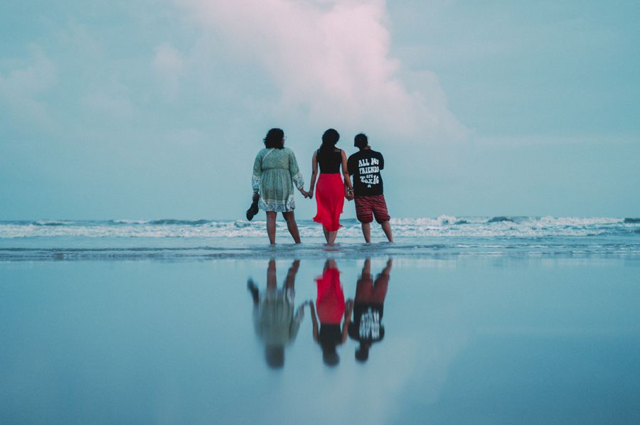 three people walking on the beach with the ocean in the background