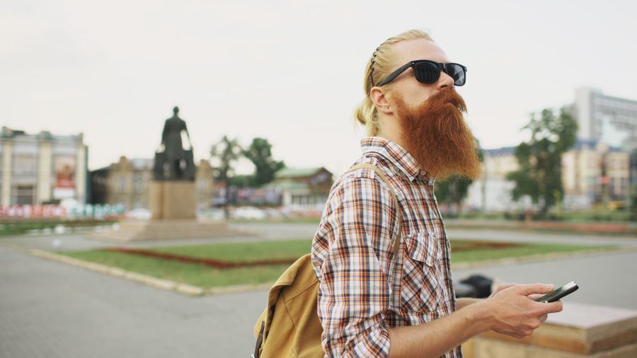 Hipster with a beard and sunglasses in a city square holding a smartphone. — Docs: Die Docs antworten, bevor Sie fragen — erst suchen, es ist schnell.