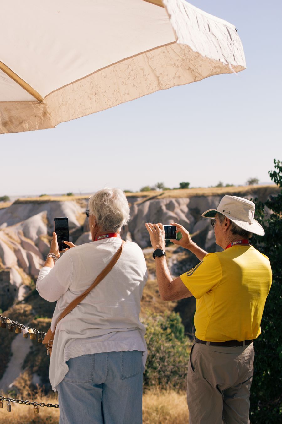 Senior tourists photographing scenic landscape in Cappadocia, Türkiye under a sun umbrella on a sunny day. — Developers: Museumsnachmittage mit streamenden Audioguides, nicht puffernd.