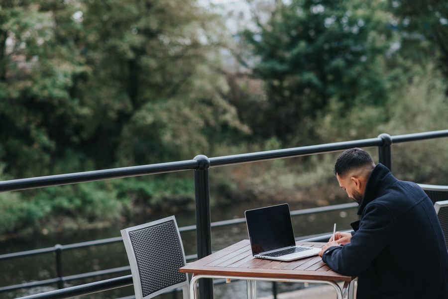 anonymous ethnic worker writing near laptop on cafe terrace — Café-Büros in Luxembourg: Hotspot stabil, kein Hotel-WLAN-Roulette.