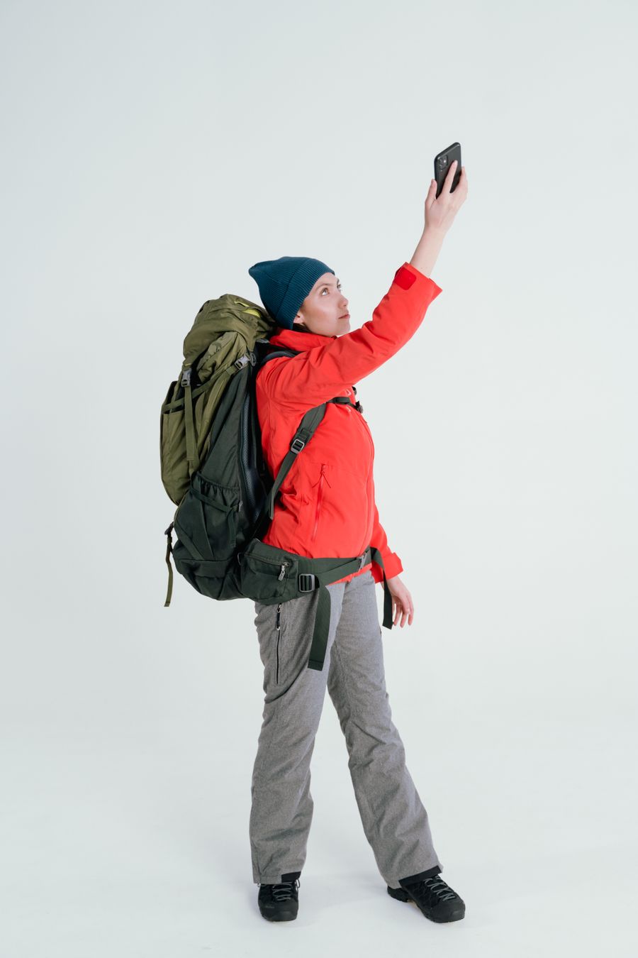 Young woman backpacker taking a selfie on a white background, dressed in outdoor gear. — Der Tele Agent führt live durch Installationen, wenn etwas stockt.