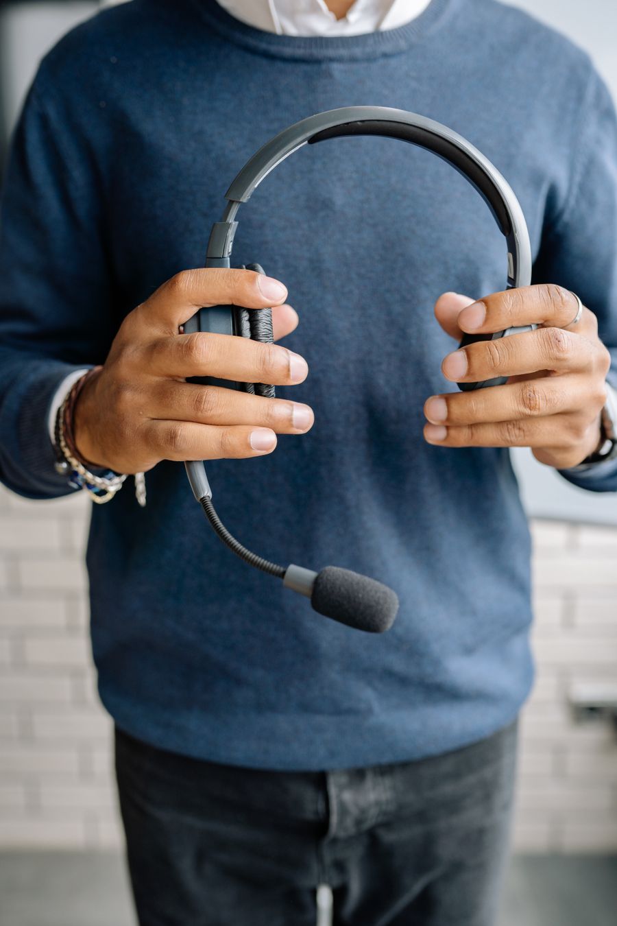 close up shot of a person in blue sweater holding a black headset — Changelog: Der Konferenz-Badge: QR-Ticket gescannt, Sessionplan synchronisiert.